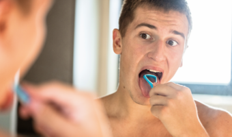 Person using a tongue scraper in the mirror.
