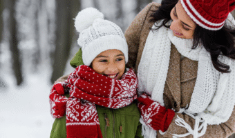 Mother and daughter smiling and wearing winter clothes, outside in the snow.