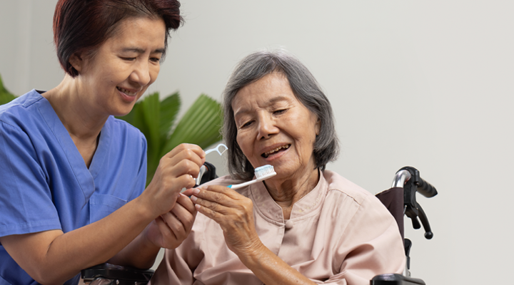 Dental assistant helping older adult brush and floss their teeth.