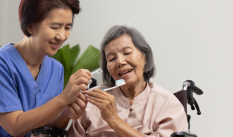 Dental assistant helping older adult brush and floss their teeth.