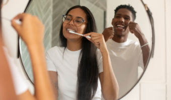 One person brushing their teeth in the mirror and another person flossing in the mirror.