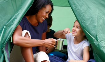 Child brushing her teeth in a tent with her mom.