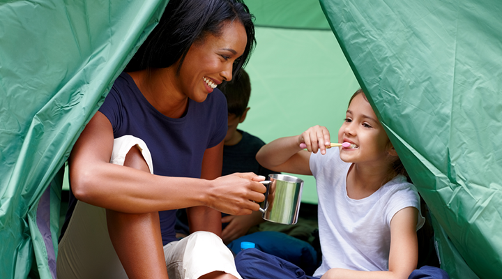 Child brushing her teeth in a tent with her mom.